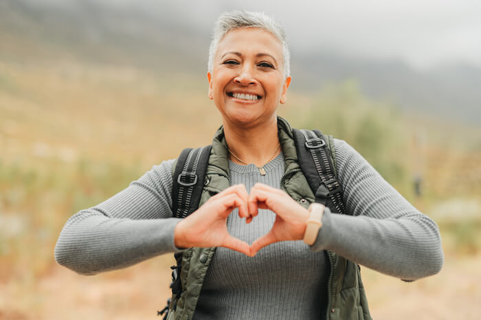 Happy woman outdoors making a heart with her hands.